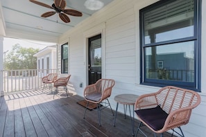 Eine überdachte Veranda mit Korbmöbeln, einem Deckenventilator und großen Fenstern.