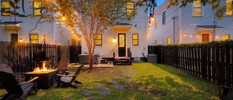 A backyard with a fire pit, outdoor seating, and string lights.