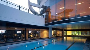 Una piscina interior moderna con paredes de vidrio y un entrepiso.