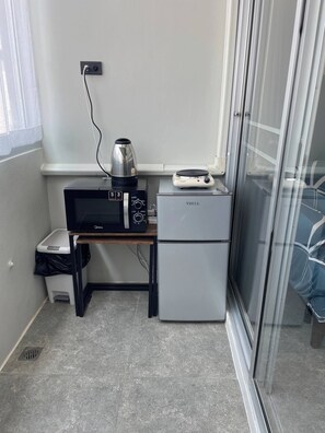 Eine Küchenzeile mit einer Mikrowelle, einem kleinen Kühlschrank, einer Kaffeemaschine und einem Mülleimer.