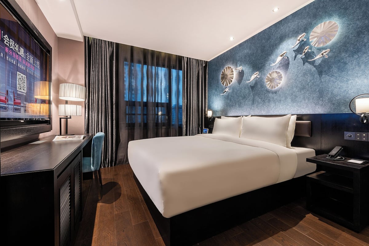 Una habitación de hotel moderna con una cama grande, un escritorio y una pantalla de televisión.