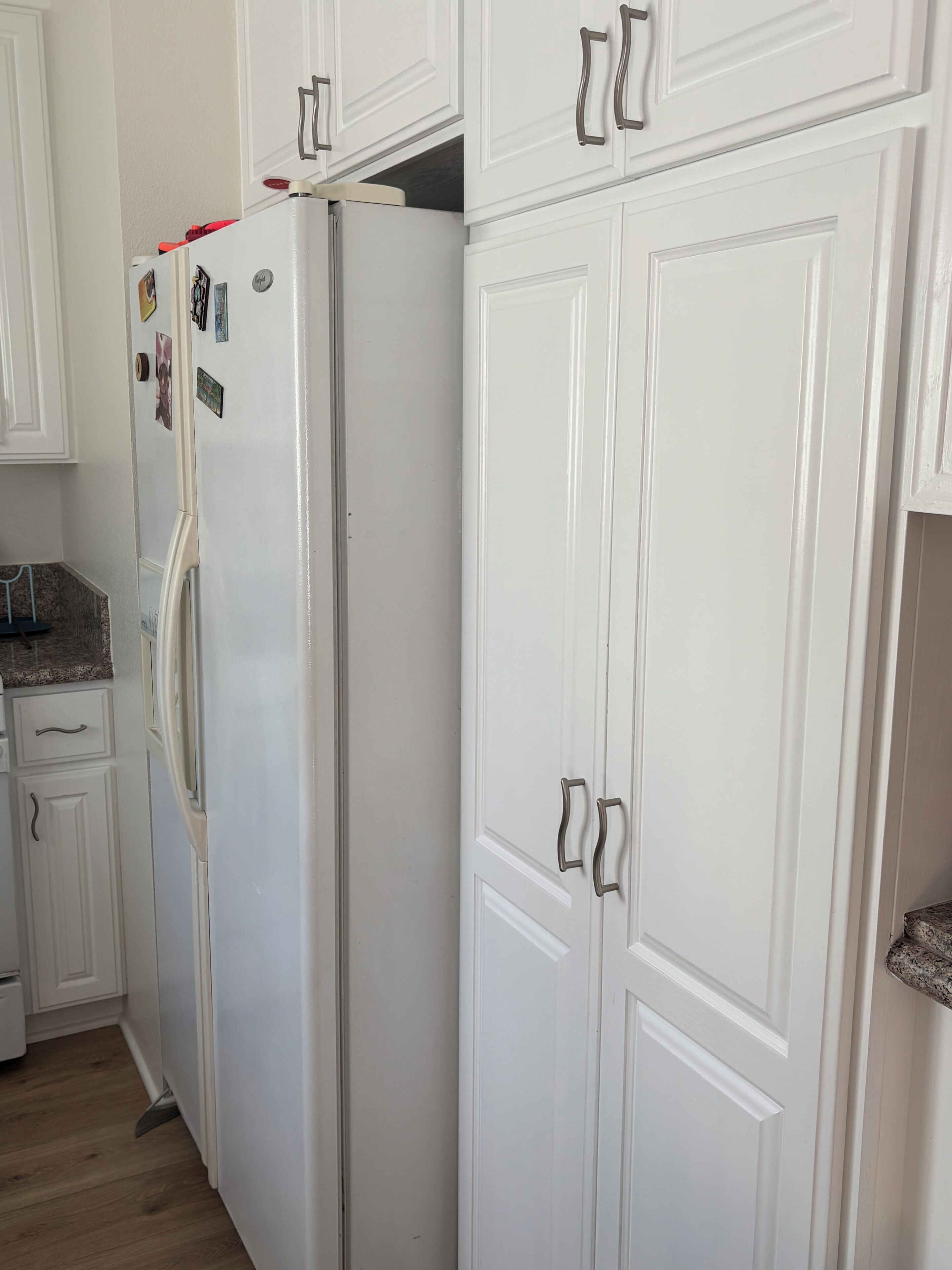A kitchen with white cabinets, a refrigerator, and a granite countertop.