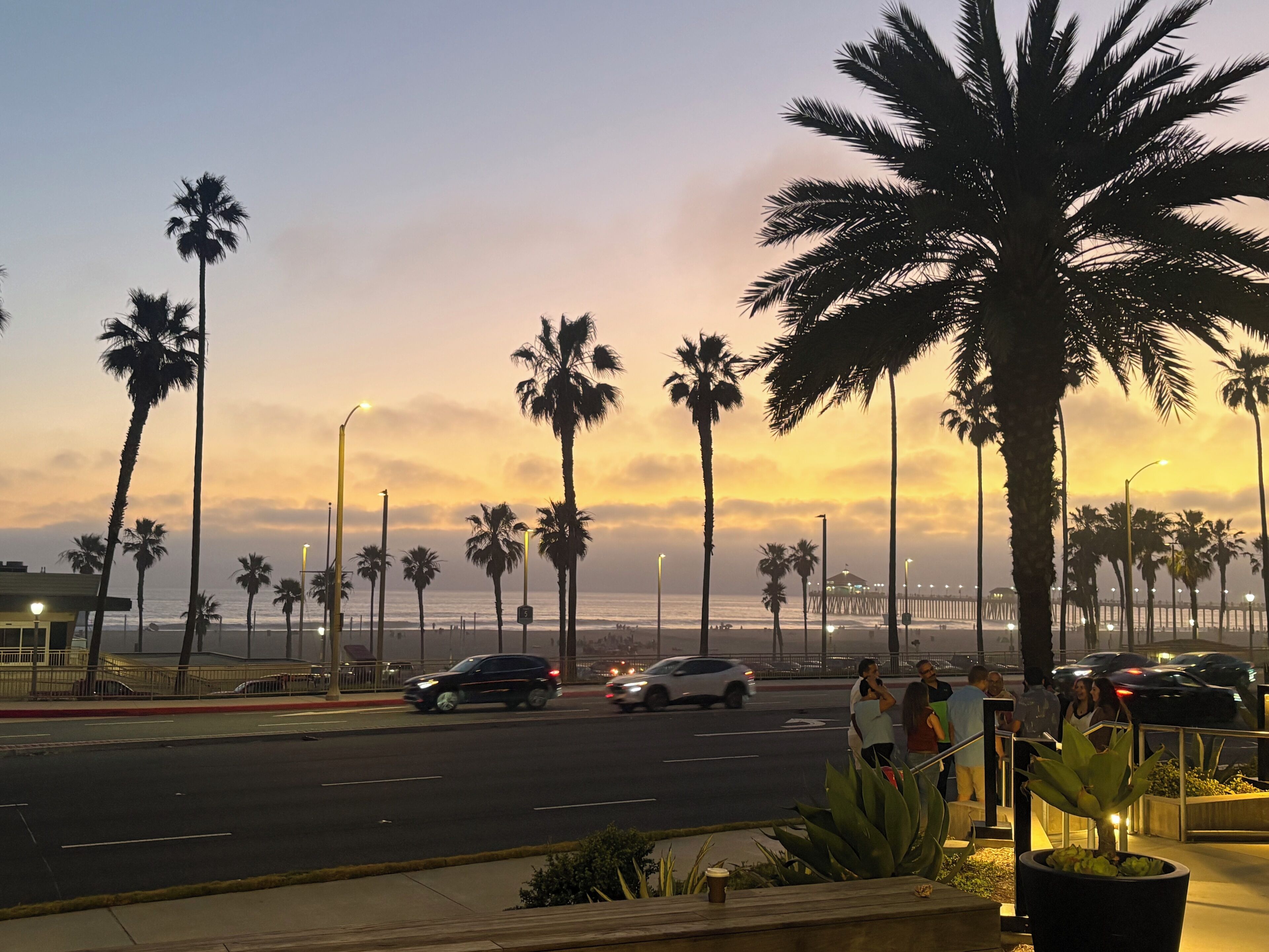 Eine Küstenstraße mit Palmen, einem Fußweg und Blick auf das Meer.
