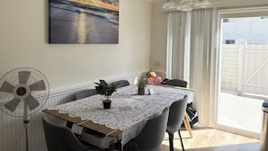 Un coin repas avec une table recouverte d’une nappe en dentelle, un ventilateur de plafond et une vue sur l’extérieur.