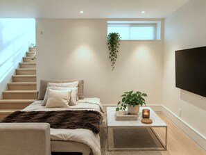 Ein modernes Schlafzimmer mit einem Bett, einem Couchtisch mit Pflanze, einem Fernseher und einer Treppe.