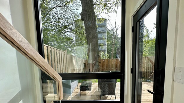 Ein Zimmer mit einem großen Fenster, einer Holztreppe und Blick auf eine Terrasse mit Gartenmöbeln.