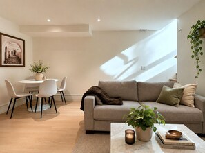Ein modernes Wohnzimmer mit einer Couch, einem Couchtisch, einem Essbereich mit Stühlen und einer hängenden Pflanze.