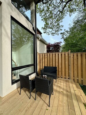 Eine Terrasse mit Gartenmöbeln und einem großen Fenster mit Blick auf einen Garten.