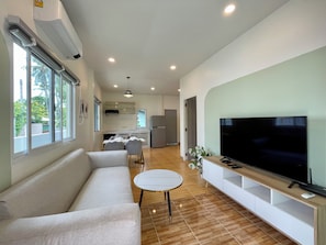 A modern living room with a sofa, a TV, and a dining area with a table and chairs. - Harmonia Residence Naiharn Phuket (Rawai)