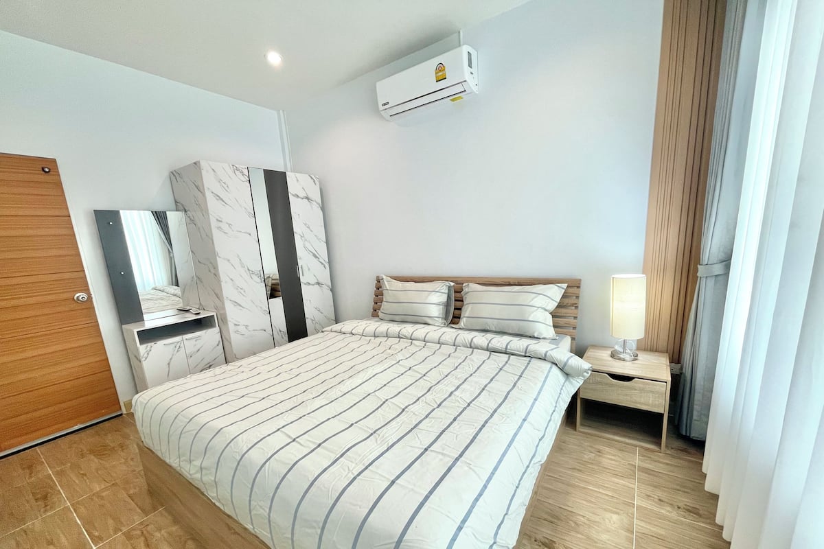 Un dormitorio con cama, mesita de noche, espejo, armario y unidad de aire acondicionado.