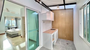 Habitación de hotel moderna con puerta de vidrio que da a un balcón, una kitchenette pequeña y vista a la ciudad.