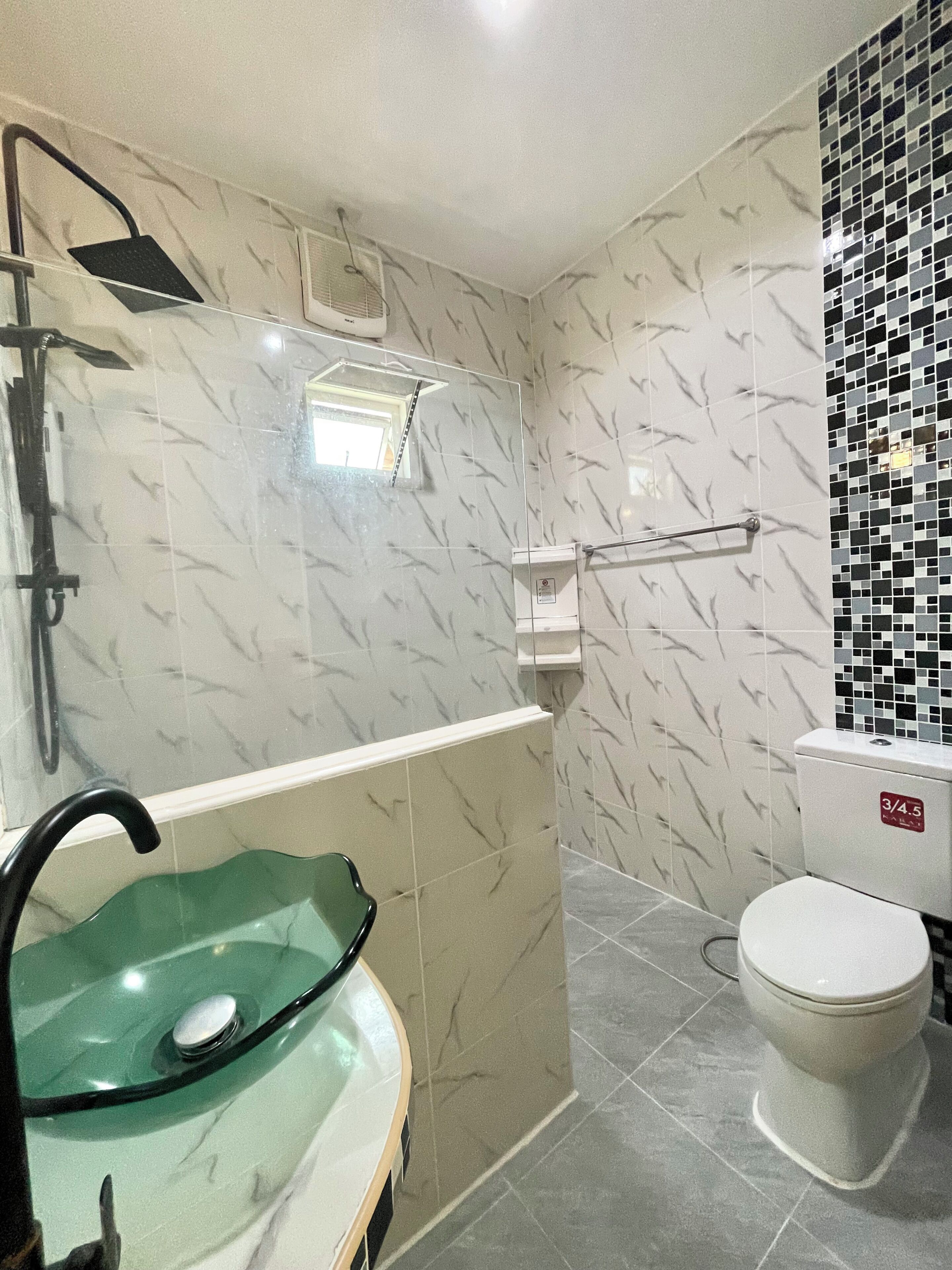Un baño con lavamanos de vidrio, ducha e inodoro.