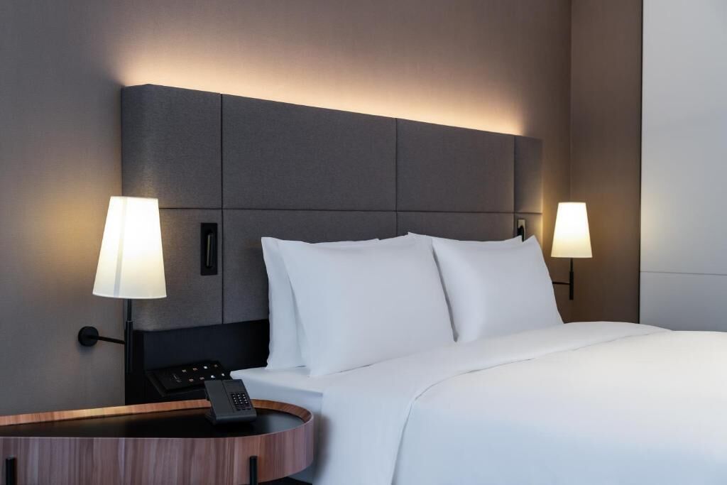 A hotel room with a large bed, two bedside lamps, a bedside phone, and a wooden side table.