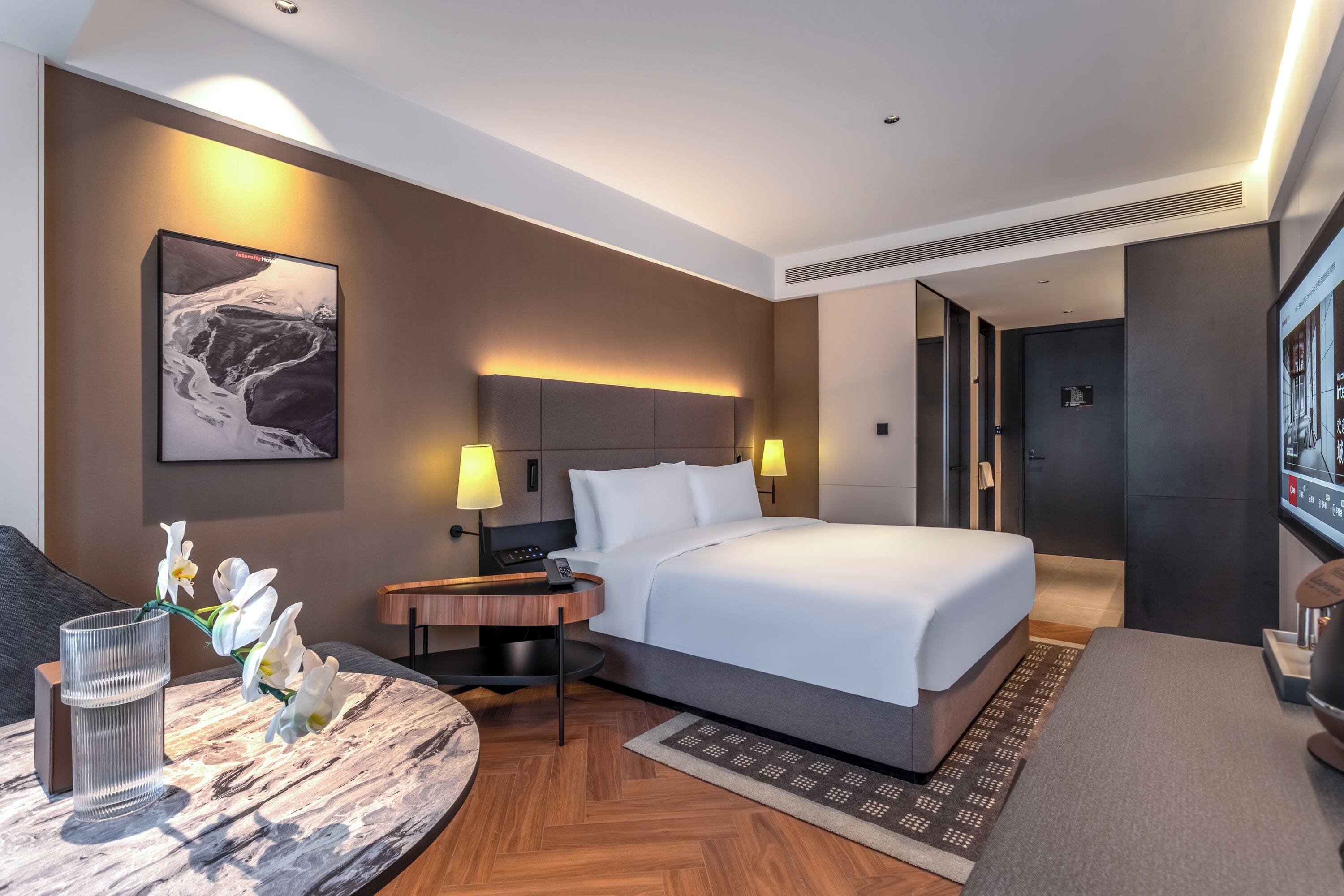 Una habitación de hotel moderna con una cama grande, mesitas de noche, un escritorio y un televisor.