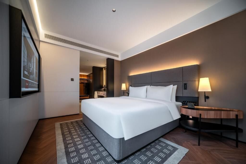 A modern hotel room with a large bed, bedside tables, a desk, and a wall-mounted TV.