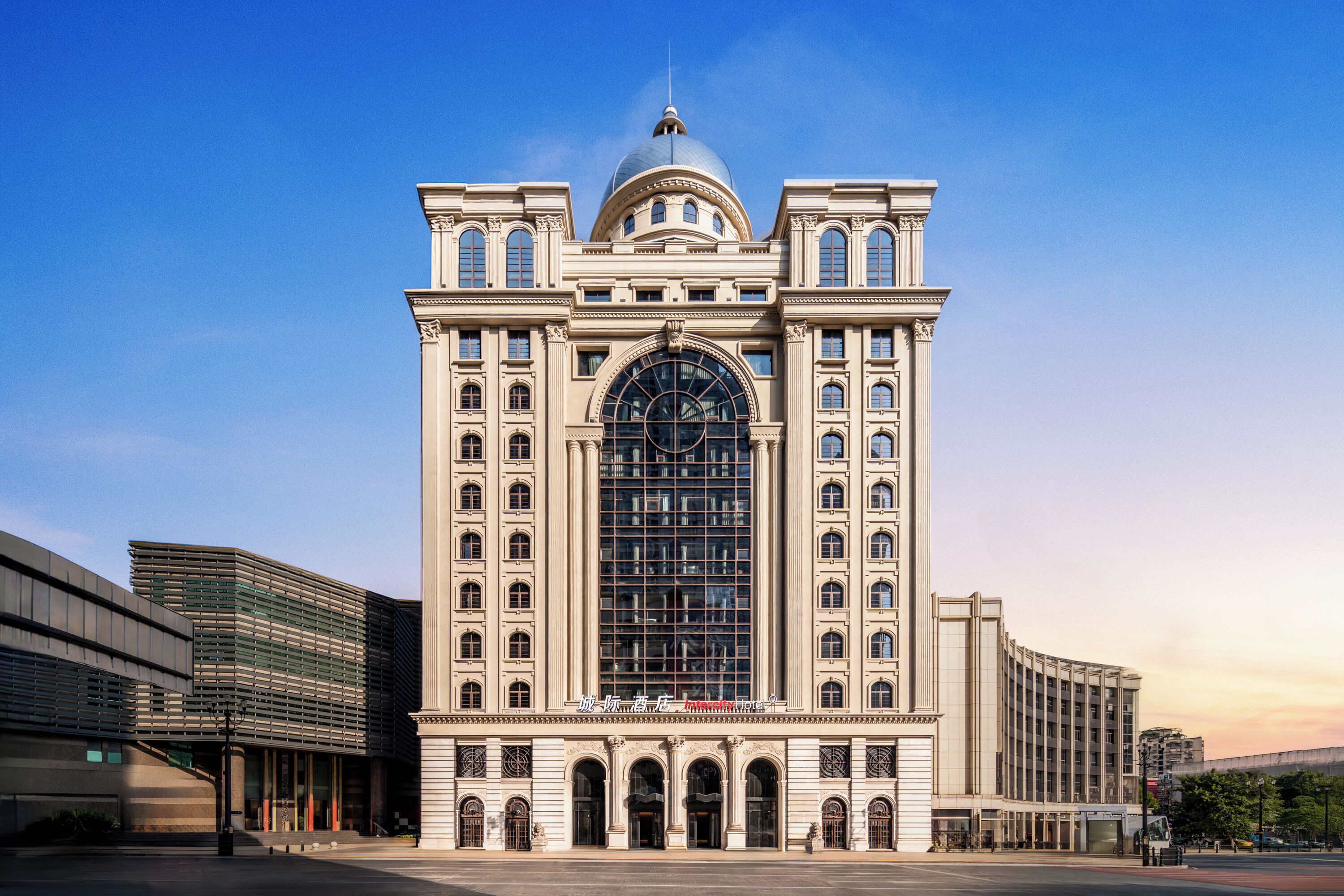 Un edificio grande de estilo clásico, con una cúpula destacada y ventanas en arco, rodeado de construcciones modernas.