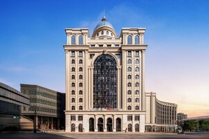 Un edificio grande de estilo clásico, con una cúpula destacada y ventanas en arco, rodeado de construcciones modernas.