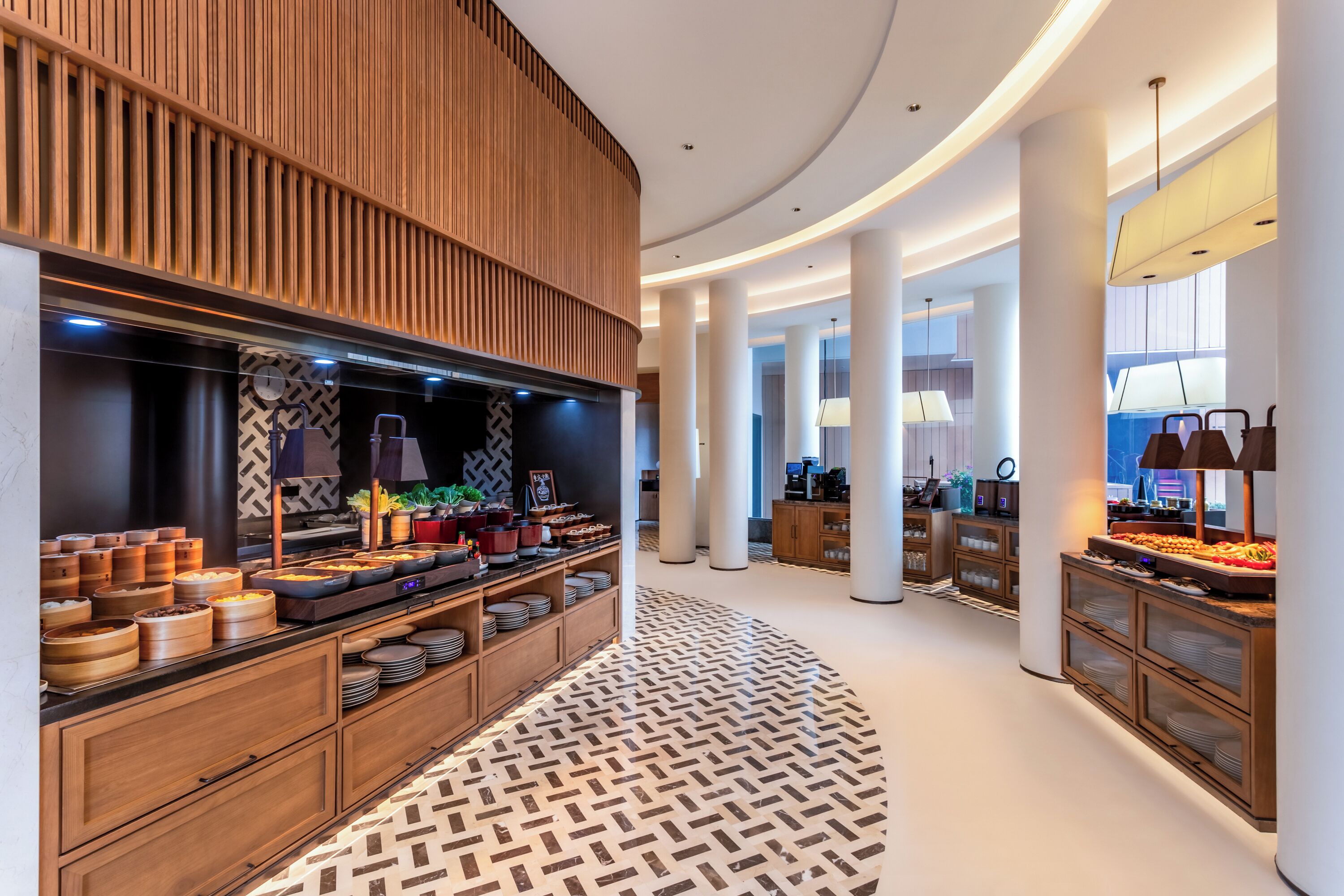 A modern hotel lobby with a buffet area, wooden paneling, and a patterned floor.