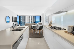 A modern kitchen with a dining area, large windows, and a view of the sea. - Ocean Front Luxe at Oracle Level 34 (Gold Coast City)