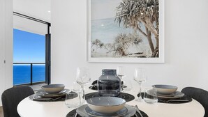 Ein Esszimmer mit Tisch, Geschirr, Gläsern und Meerblick durch ein großes Fenster.