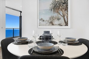 A dining table set with plates, bowls, and glasses, with a view of the ocean through a large window. - Ocean Front Luxe at Oracle Level 34 (Gold Coast City)