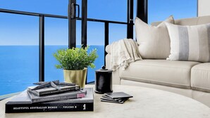 Ein Zimmer mit Meerblick, eine Couch, ein Couchtisch mit Büchern und einer Pflanze sowie ein schwarzer Behälter.