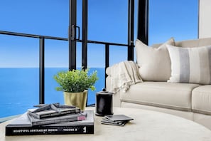 A room with a view of the ocean, a sofa, a coffee table with books and a plant, and a black container. - Ocean Front Luxe at Oracle Level 34 (Gold Coast City)