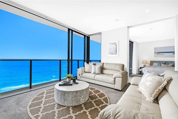 A modern living room with a large window overlooking the ocean, a round coffee table, and a beige sofa. - Ocean Front Luxe at Oracle Level 34 (Gold Coast City)