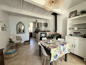 Une cuisine avec des meubles blancs, une table à manger recouverte d’une nappe colorée et un poêle noir.