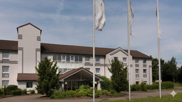 Ett modernt hotell med en symmetrisk fasad, flera flaggstänger och en central huvudentré.