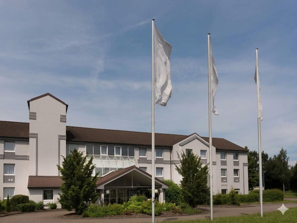 Un hotel moderno con fachada simétrica, varios mástiles de bandera y una entrada central.