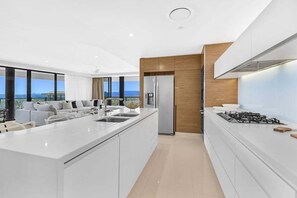 A modern kitchen with a central island, a built-in oven, and a large window overlooking a cityscape. - Mega Ocean View Skyhome at Oracle Level 37 (Gold Coast)