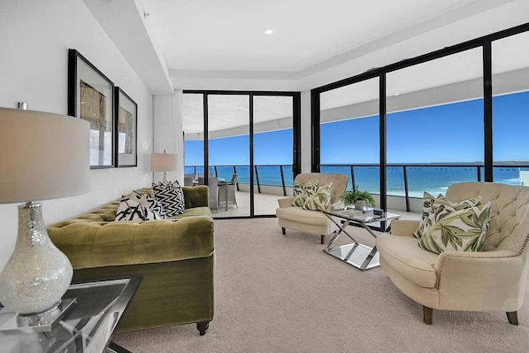 A spacious living area with a large window overlooking the ocean, a green sofa, a beige armchair, and a coffee table. - Mega Ocean View Skyhome at Oracle Level 37 (Gold Coast)