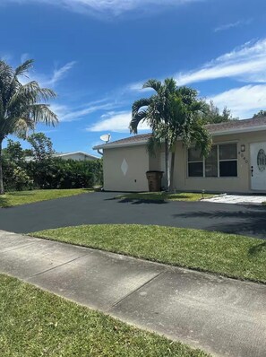 A residential property with a paved driveway, a lawn, and a palm tree.