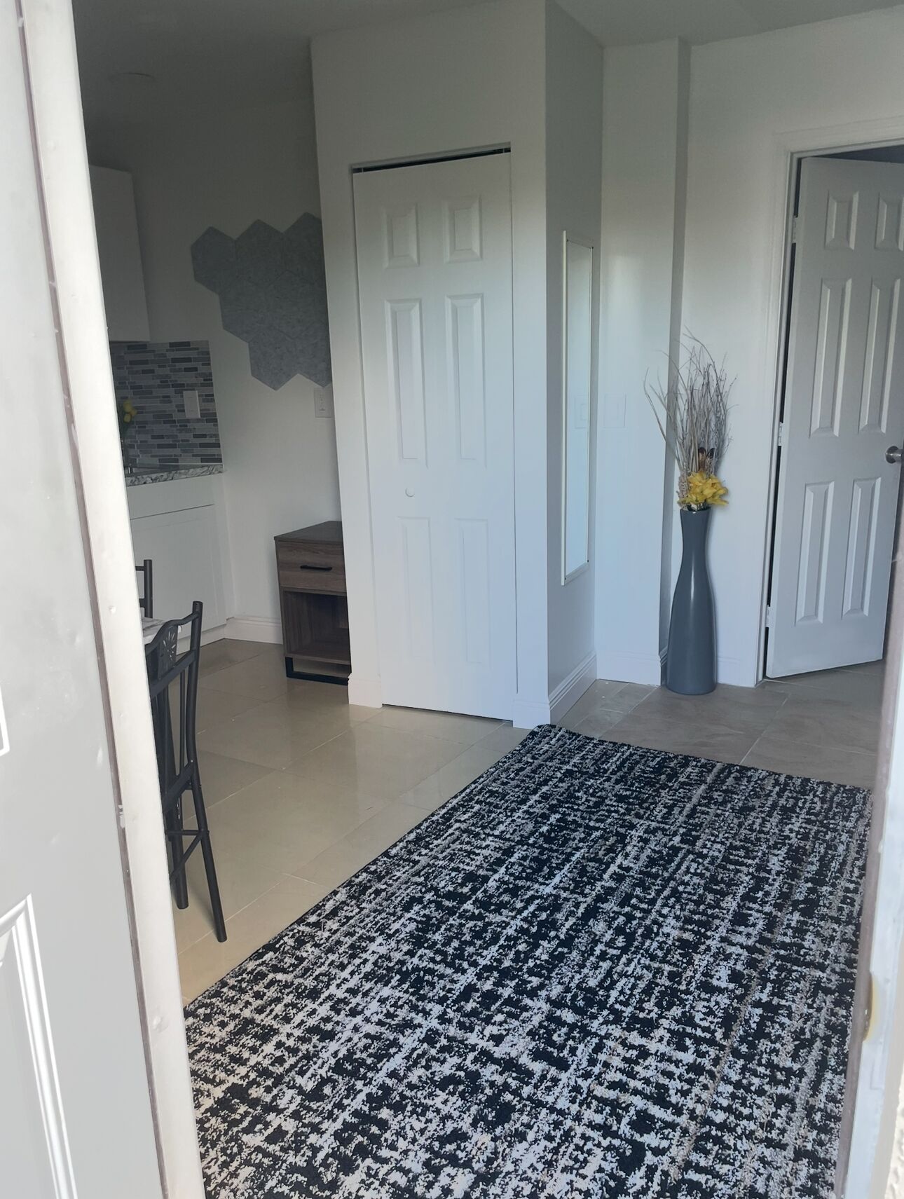 A hallway with a patterned rug, a door, a vase with flowers, and a wall-mounted artwork.