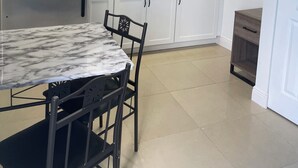 Eine moderne Küche mit weißen Schränken, einem Edelstahlkühlschrank, einer Mikrowelle, einer Marmorarbeitsplatte und einem Essbereich mit Tisch und Stühlen.