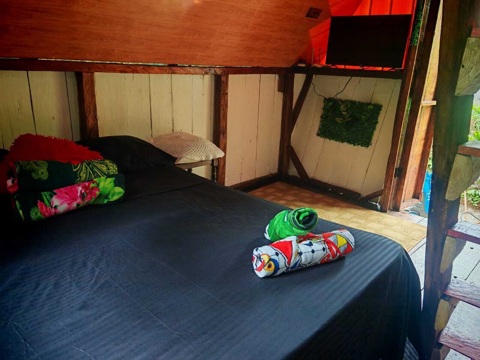 Uma cama de solteiro com lençol preto, travesseiro colorido e um cobertor enrolado com um personagem de desenho animado.