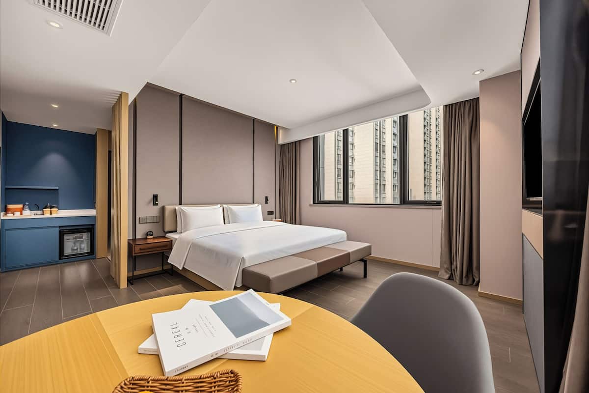 A modern hotel room with a bed, bedside table, and a view of the city.