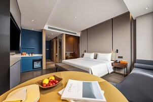 Una habitación de hotel moderna con cama, mesita de noche y una pequeña kitchenette.