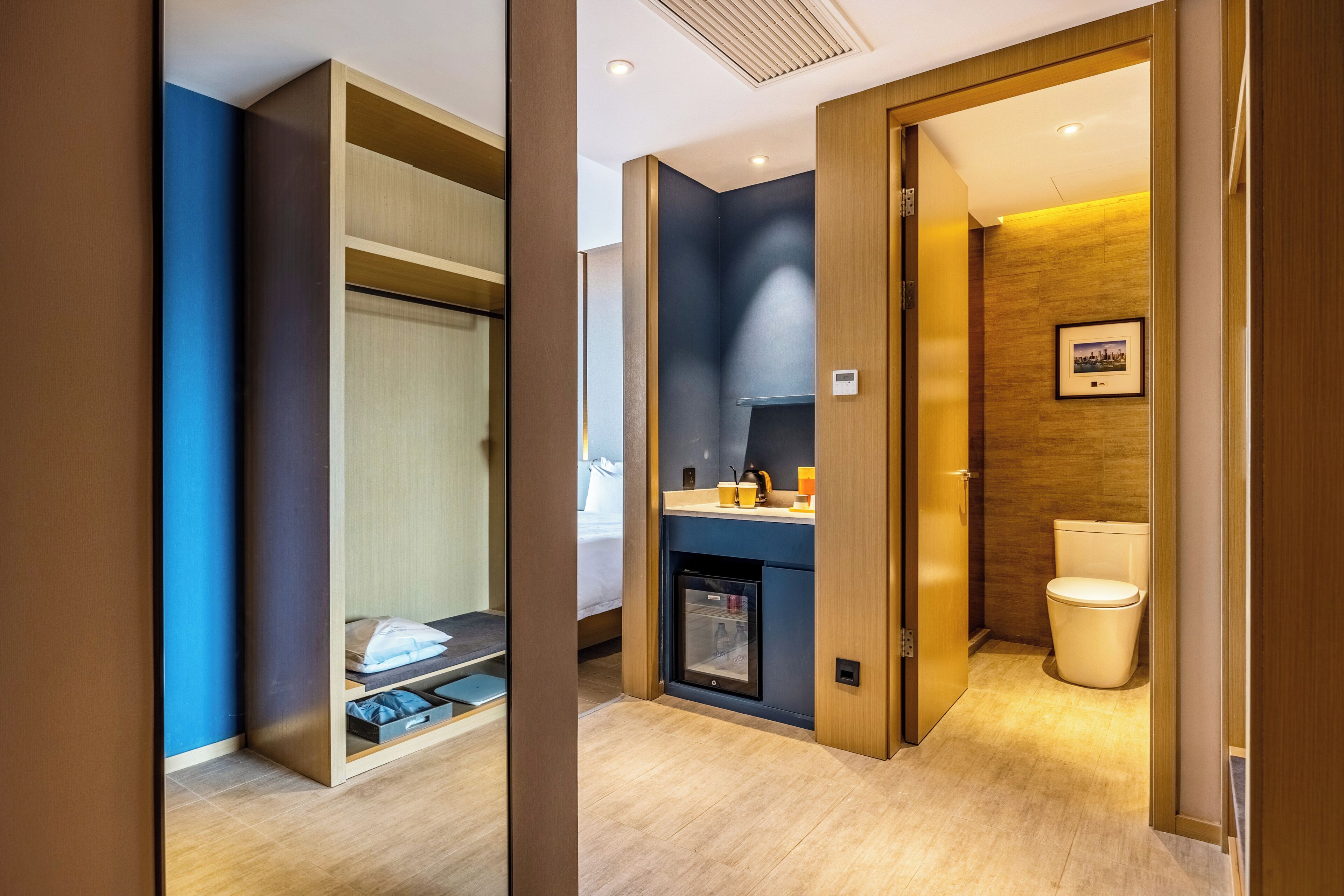 Ein modernes Hotelzimmer mit Bett, eingebautem Kleiderschrank, Küchenzeile und Toilette.