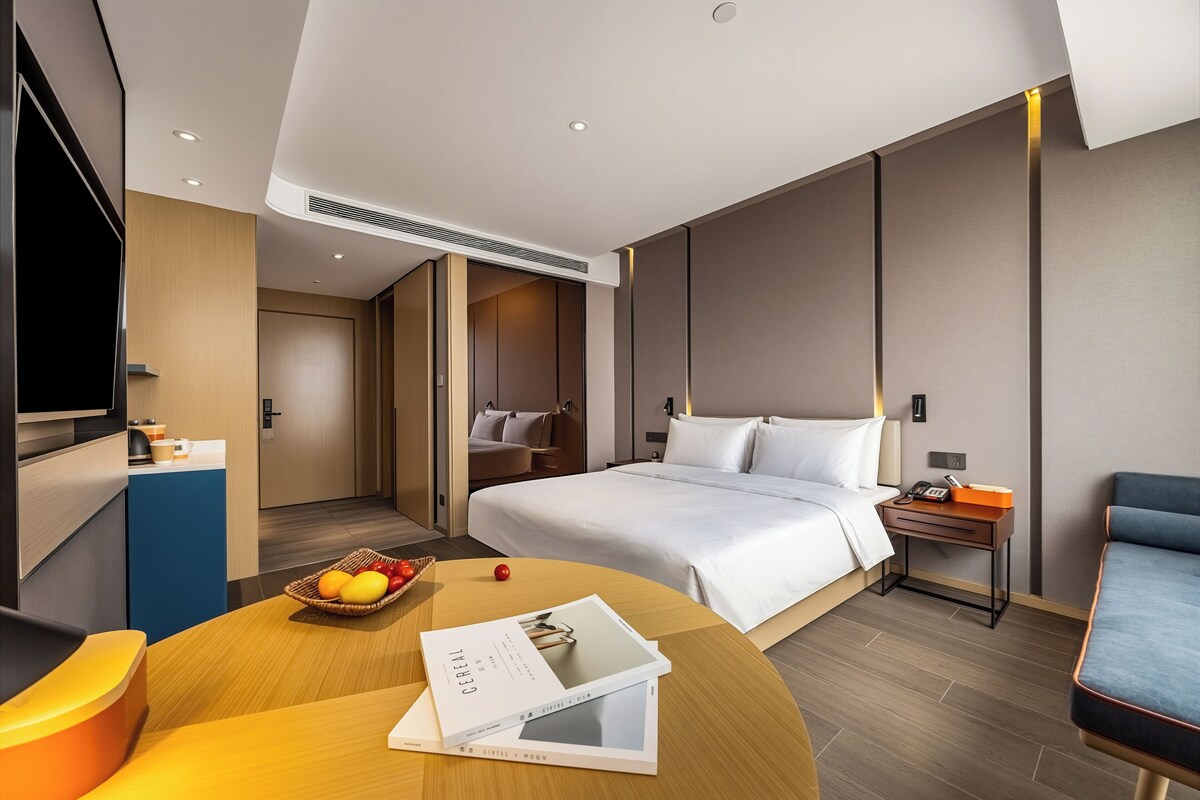 A modern hotel room with a bed, bedside table, TV, and a small desk area.