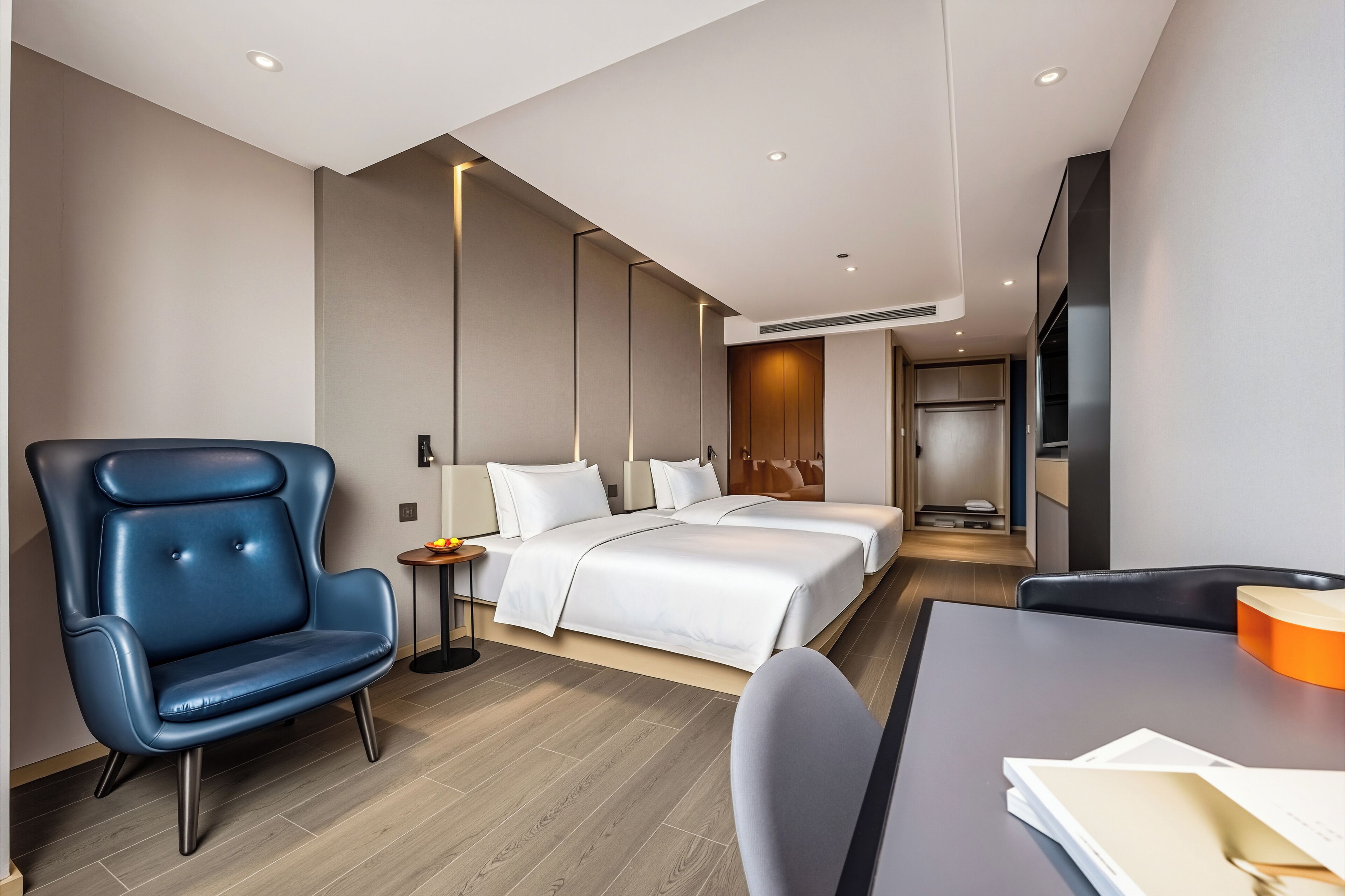 Ein modernes Hotelzimmer mit einem großen Bett, einem blauen Sessel, einem Schreibtisch und einem Fernseher.
