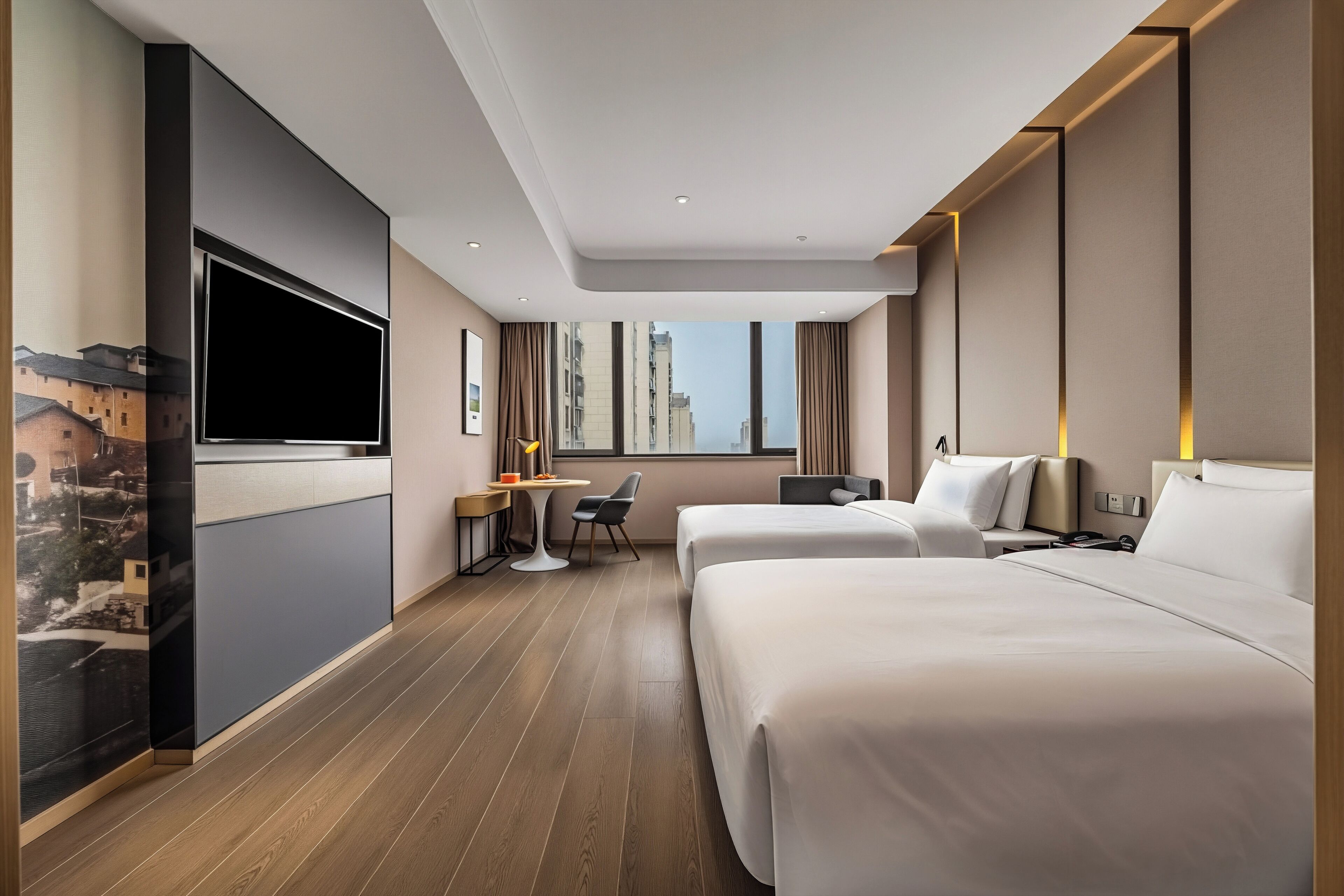 A hotel room with two beds, a desk, a chair, a TV, and a window with a city view.
