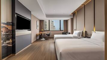 A hotel room with two beds, a desk, a chair, a TV, and a window with a city view.