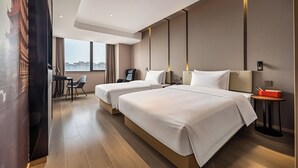 Une chambre d’hôtel avec deux lits, un bureau avec une chaise, une petite table avec une lampe et une vue sur la ville.