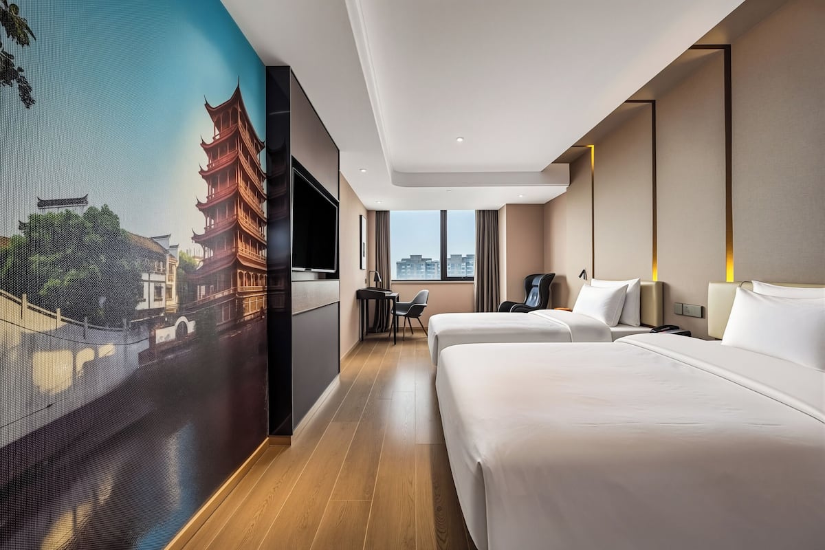 A hotel room with a large wall mural, two beds, a desk, and a chair.