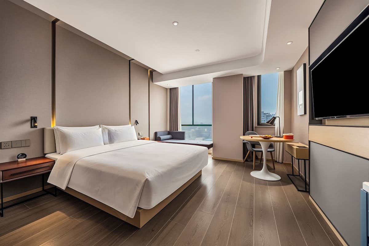 A modern hotel room with a large bed, a desk, a chair, and a TV.