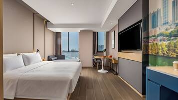 Habitación de hotel moderna con una cama grande, un escritorio, una silla, un televisor de pantalla plana y vistas a la ciudad.