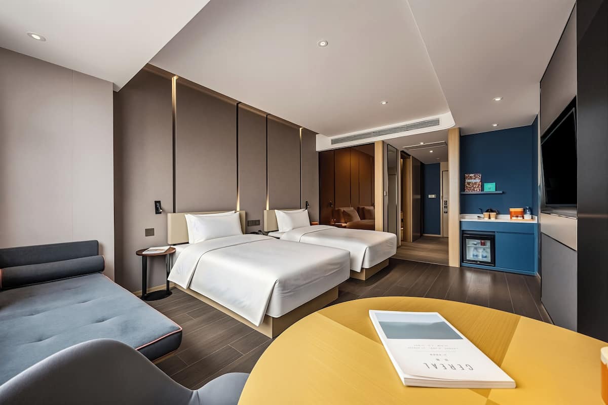 A hotel room with two beds, a sofa, a small table, and a kitchenette.