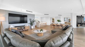 Una sala de estar moderna con un televisor de pantalla plana grande, sofás de cuero, una mesa de centro y un comedor con muebles de madera.